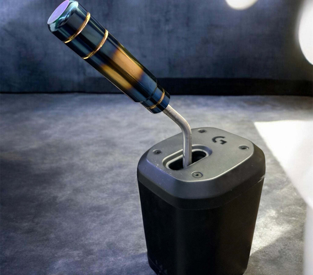 Logitech RS Shifter with a black base and an angled stainless steel S-shaped stick topped by a black handle with gold accents.